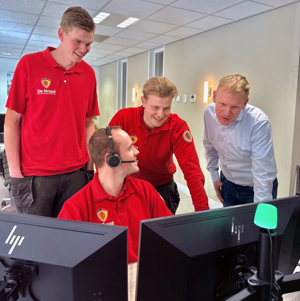Vier collega's zitten en staan aan een bureau met computers.
