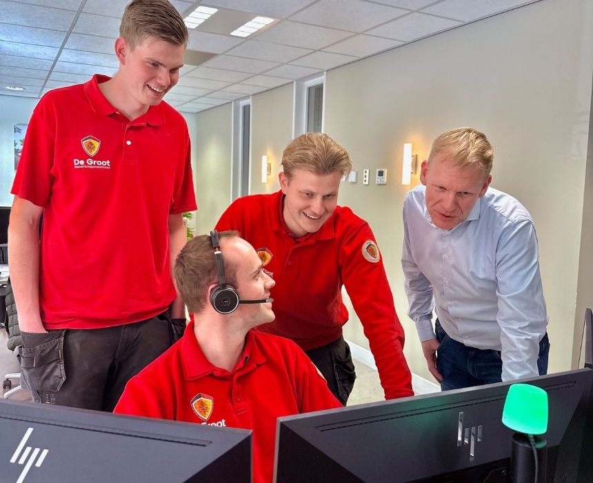 Vier collega's staan samen bij computer en overleggen en lachen.