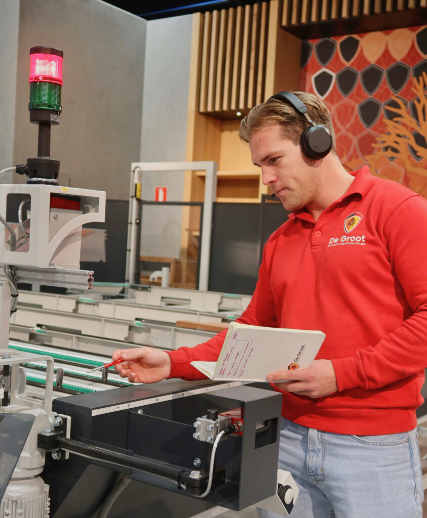 Servicecenter technici De Groot wijst naar machine met pen met koptelefoon op